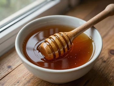Overhead close-up of a ceramic bowl filled with dark amber raw honey, natural daylight from a north-facing window, wooden honey dipper resting on the rim, rustic wooden surface beneath