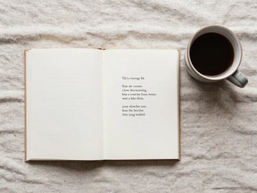Overhead flat-lay of a small poetry book open on a textured linen sheet next to a ceramic cup of coffee