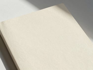 A close-up of a physical book cover resting on textured cream paper, soft shadows, natural light