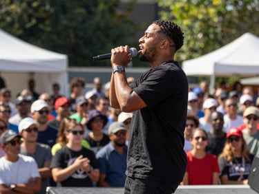 A slam poet performing passionately on a sunlit outdoor stage, microphone in hand, crowd visible in the background, documentary style.