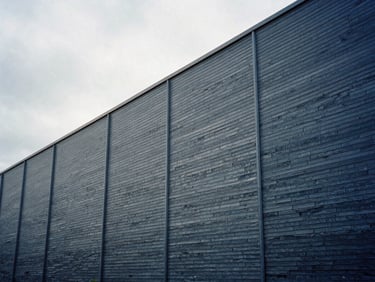 Industrial manufacturing facility exterior, metallic cladding, cool slate tones under overcast UK sky, clean architectural lines, 35mm
