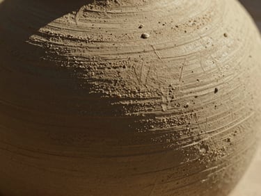 Extreme macro close-up of hand-carved clay texture showing deep chisel marks and raw mineral grain, warm grazing sunlight highlighting the physical weight.