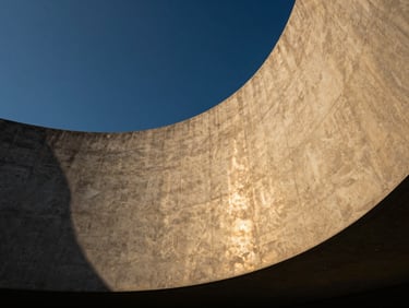 Low-angle architectural photography of a modern concrete facade with sweeping curves, deep blue sky, golden hour light reflections