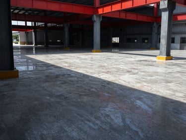 Wide shot of a finished industrial concrete floor with brilliant light reflection, steel columns of a warehouse framing the scene