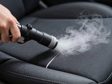Close-up of a professional steam extraction nozzle cleaning a dark fabric car seat, clean line separating treated and untreated areas