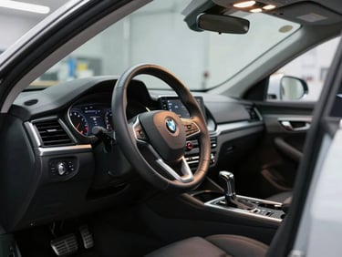 An open car door showing a perfectly detailed leather steering wheel and clean dashboard console under bright clinical workshop light