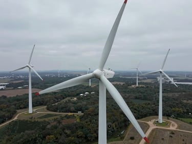 Top-down orthographic drone photograph of an industrial wind turbine array in overcast daylight, crisp technical lines.