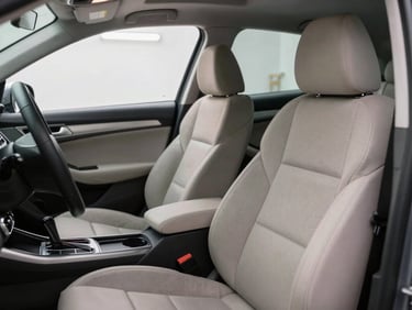 Interior of a car with seats and door panels being dry cleaned using equipment, bright workshop lighting from overhead, close view showing the cleaning process on fabric upholstery