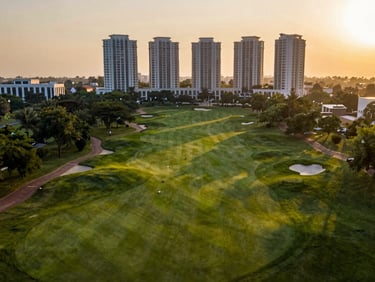 Golden hour drone perspective of M3M Golf Estate, Gurugram, expansive green golf course integrated with premium high-rise architecture, warm soft light