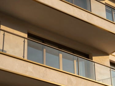 Close-up architectural detail of a modern luxury balcony with champagne gold trim, warm sunset light casting geometric shadows.