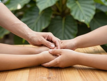 A founder's hands gently guiding a student's hands in a teaching position, natural wood table, soft natural daylight, deep botanical greens and gold tones, shallow depth of field, 35mm.