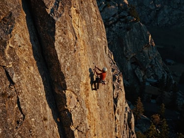 Dramatic wide shot of a climber ascending a rock face in the Wasatch Front, golden hour lighting, cinematic film grain, product visible.