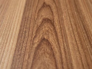 Macro close-up of polished teak wood grain, tight annual rings and hand-planed surface visible in north-facing daylight, straight-on product study framing