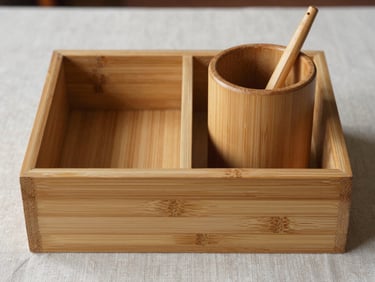 Close-up straight-on study of a finished bamboo desk organiser and a hand-turned wooden pen holder side by side on a raw linen surface, north-facing daylight raking across the bamboo joints and wood grain, no props or office context, material texture as sole subject