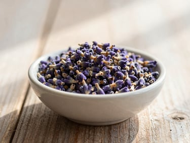 Culinary lavender buds in a small handmade ceramic bowl on a rustic wooden table, soft morning sun