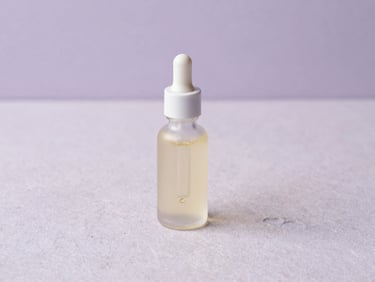 Elegant glass dropper bottle with lavender oil on a light purple stone surface, soft morning light, minimalist flat-lay