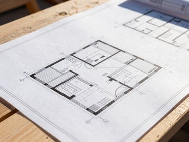 Architectural blueprints laid out on a clean job site table, close-up, focused on details, bright natural Alberta daylight, high-contrast, 35mm lens.