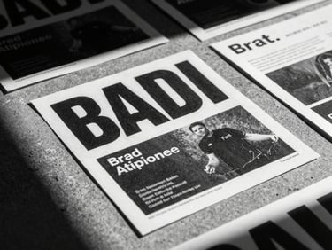 Extreme close-up, high-contrast black and white photo of printed campaign mockups on a raw concrete floor, harsh direct flash, heavy shadow.