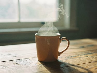 Soft warm golden-hour window light hitting a single ceramic mug on a rustic wooden table, steam rising gently, shallow depth of field, 35mm film