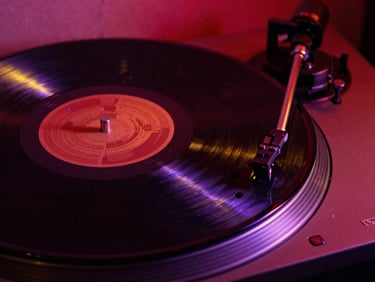 Close-up of a vinyl record spinning on a turntable, moody crimson backlighting, dust particles illuminated in gold, raw street-level aesthetic.
