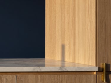 Minimalist interior detail showing premium materials, a marble countertop reflecting soft twilight glow, brass fittings, and clean oak paneling