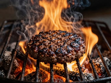 Moody food photography of a juicy burger patty grilling on open flames, rich golden highlights from the fire, deep shadows, smoke rising, 35mm film texture