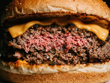 Macro close-up of a sliced artisanal burger showing a perfectly cooked juicy pink center, melted cheese dripping, warm low-key lighting, deep shadows, 35mm film texture