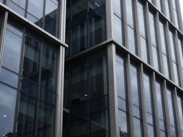 Architectural closeup of a modern corporate building facade with sharp steel and glass angles, cool overcast daylight, deep navy reflections, 35mm