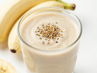 Creamy almond butter and banana smoothie topped with hemp seeds, bright high-key lighting, clean slate background