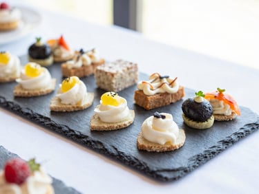 Elegant, clean plating of gourmet appetizers on a slate tray at a corporate event, bright natural lighting, soft daylight with shallow depth of field