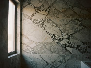 Luxury bathroom wall featuring perfectly book-matched Calacatta marble panels, soft natural window light, architectural perspective
