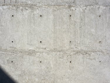 Raw textured concrete wall with formwork tie holes, harsh natural light casting sharp shadows, high contrast, 35mm