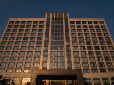 Symmetrical architectural wide shot of a modern luxury hotel facade in Delhi NCR, dusk lighting, deep navy sky, crisp reflections