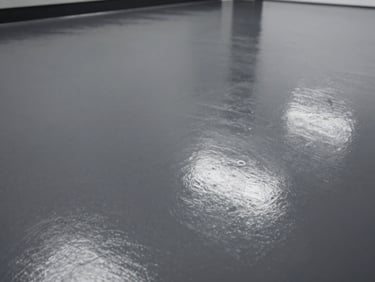 Close-up, high-contrast shot of a dark gray epoxy floor, showing a seamless, reflective surface under bright industrial lighting, low angle.