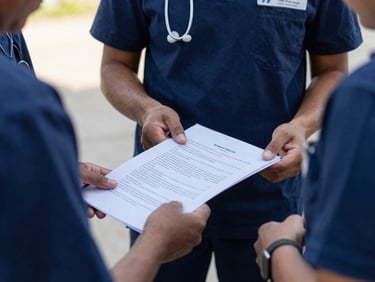 Gros plan sur les mains d'un membre de l'équipe transmettant un document officiel et des fournitures médicales à un partenaire local, lumière naturelle, ton bleu marine.