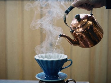 Hands pouring hot water from a copper kettle into a ceramic dripper, steam rising, warm wooden background, moody film photography