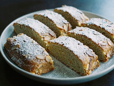 Slices of traditional almond cake on a ceramic plate, powdered sugar dusting, warm cozy interior lighting, 35mm lens
