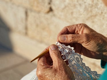 Extreme close-up of delicate lace being handmade with wooden bobbins by an elderly woman's hands, warm limestone background, soft focus, 35mm.