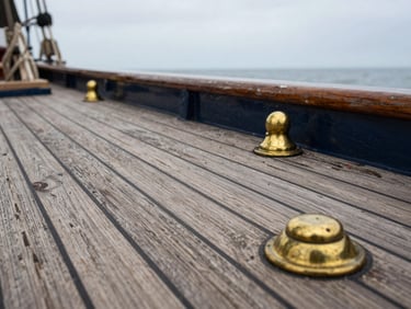 Macro shot of weathered teak decking on a classic ship, brass fittings, soft overcast coastal light, detailed wood grain