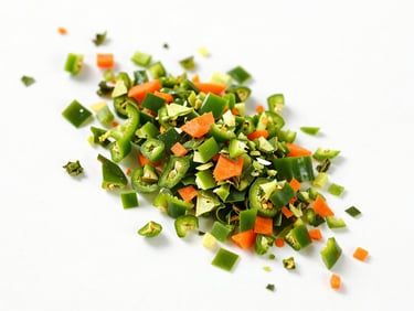 High-key overhead shot of dehydrated green bell pepper flakes and carrot granules on a clean white surface.