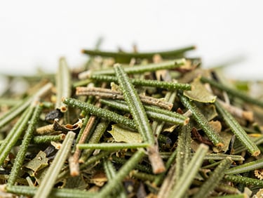 Macro close-up of dried green herb flakes and rosemary needles, crisp natural daylight, showing fine leaf textures