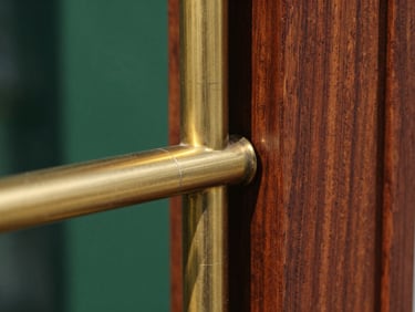 Extreme close-up of brushed brass hardware meeting dark raw walnut grain, sharp natural daylight, deep shadows