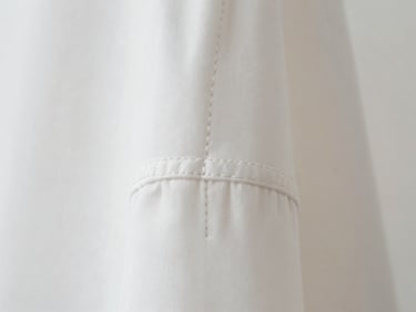 Macro close-up of a perfectly stitched seam on a white garment, showcasing the clean lines and craftsmanship, soft studio lighting.