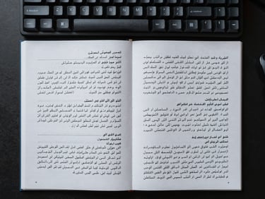 Close overhead flat-lay of a workstation: annotated bilingual text document with Arabic and Chinese script side by side, handwritten margin notes visible, mechanical keyboard in the upper corner, cool even studio light, sharp focus on annotation marks