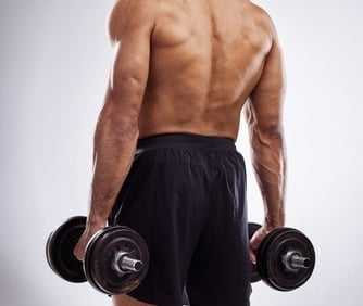 Rear view of a muscular man holding heavy dumbbells for back and shoulder strength training.
