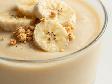 Overhead close-up of banana pudding in a glass dish, thick vanilla-flecked custard layers, soft vanilla wafer crumbs, warm natural light, shallow depth of field.