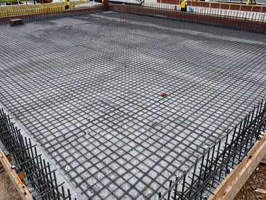 Overhead view of a large residential development foundation slab under overcast daylight, rebar grid precisely laid on formwork, no people, material honesty in concrete and steel