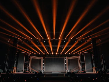 Massive event stage structure with intricate lighting setup, wide-angle view, dramatic high-contrast, deep blacks with orange spotlights, architectural lines, sharp details, 35mm