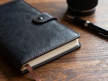 A close-up detail of a structured leather notebook and a fountain pen on a heavy oak desk, dramatic side lighting, sharp shadows.