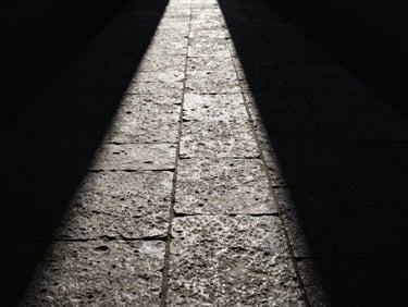 Dramatic chiaroscuro photography of a stark stone path splitting into light and deep shadow, single-source illumination, 35mm film grain, minimalist symbolic horizon.